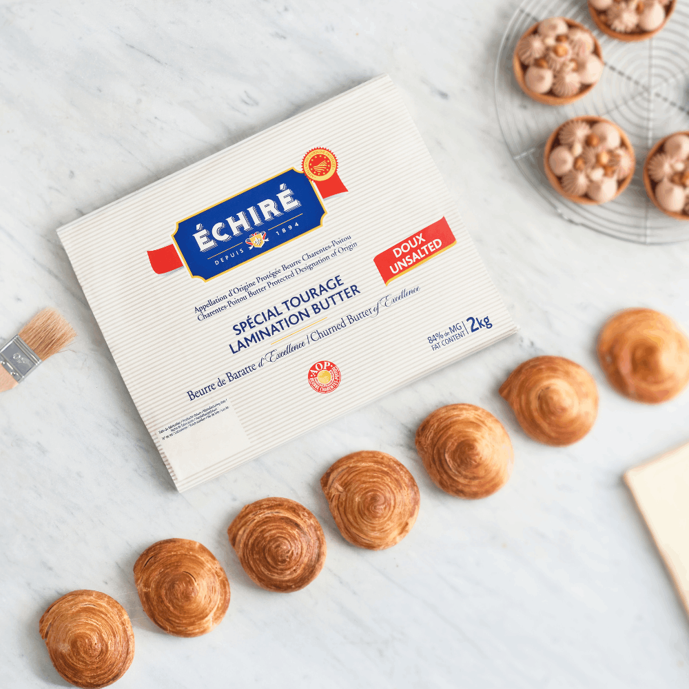 Echiré Beurre de Tourage lamination butter for croissants and pastries, displayed with baked viennoiseries on a marble surface.