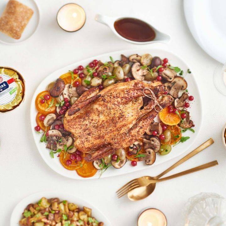 Roast chicken with vegetables and Échiré 250g French butter in wooden basket on an elegant dining table.