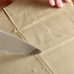 Cutting sheet of butter puff pastry dough into squares for baking pastries