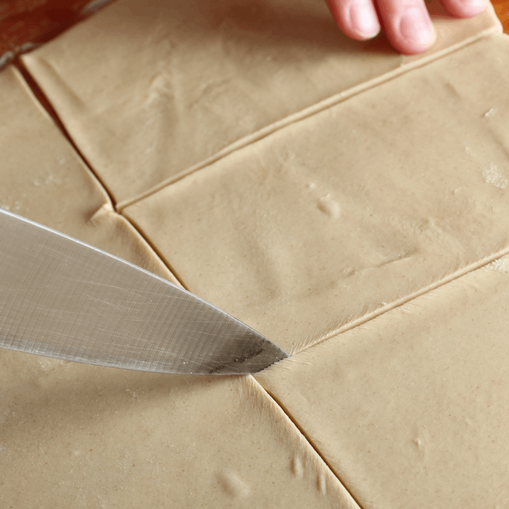 Cutting a sheet of puff pastry dough with a knife for baking pastries