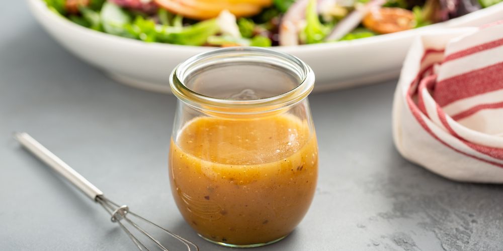 Homemade verjus vinaigrette served in a glass jar with a fresh green salad in the background.