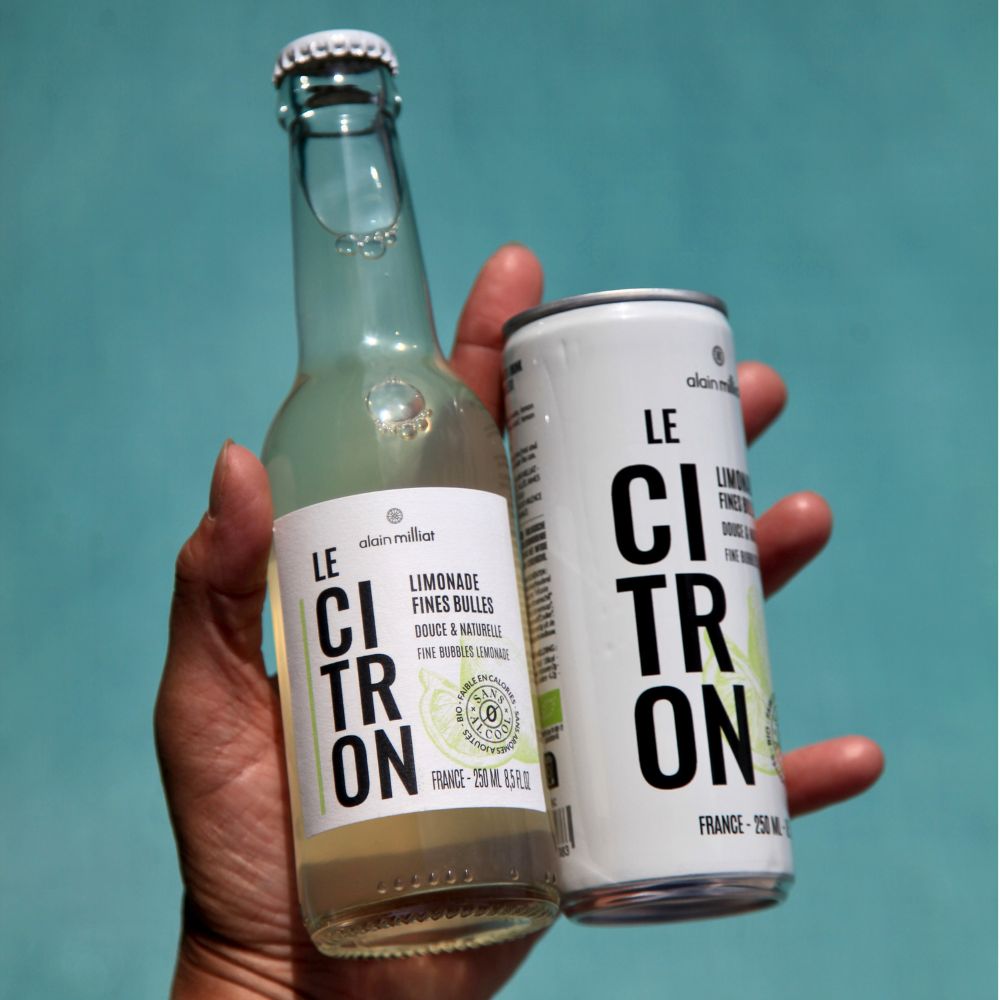 Alain Milliat fine bubbles lemonade 250ml bottle and can held together outdoors in a lifestyle setting