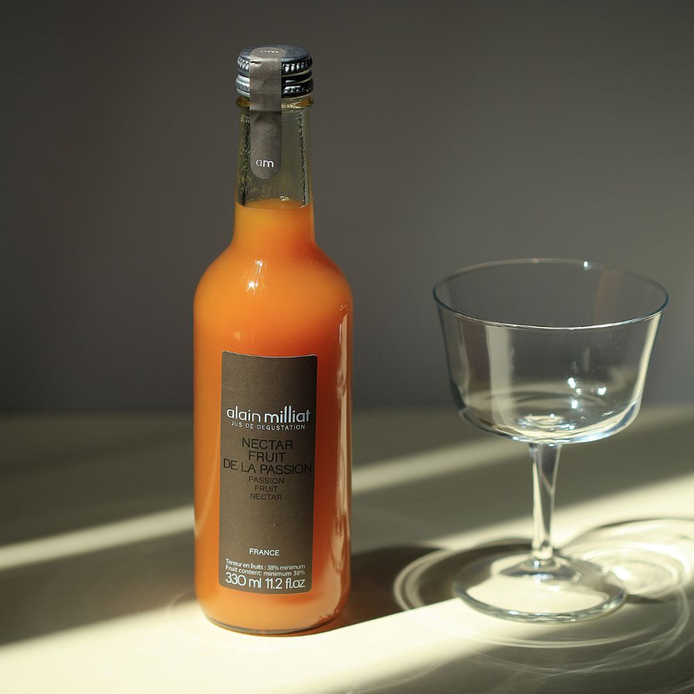 Alain Milliat passion fruit nectar 330ml bottle displayed beside a cocktail glass in soft natural light