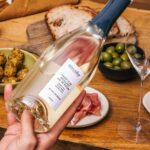 Alain Milliat sparkling Pinot Noir grape juice 750ml bottle held above a table with appetisers and glassware in a lifestyle setting