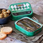 Ferrigno Small Mackerel in Olive Oil 135g shown in an open tin with olives and sliced bread