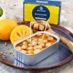 Serving suggestion showing an open 120 g tin of Ferrigno Beau Rivage squid with preserved lemon on a plate with lemons and herbs.
