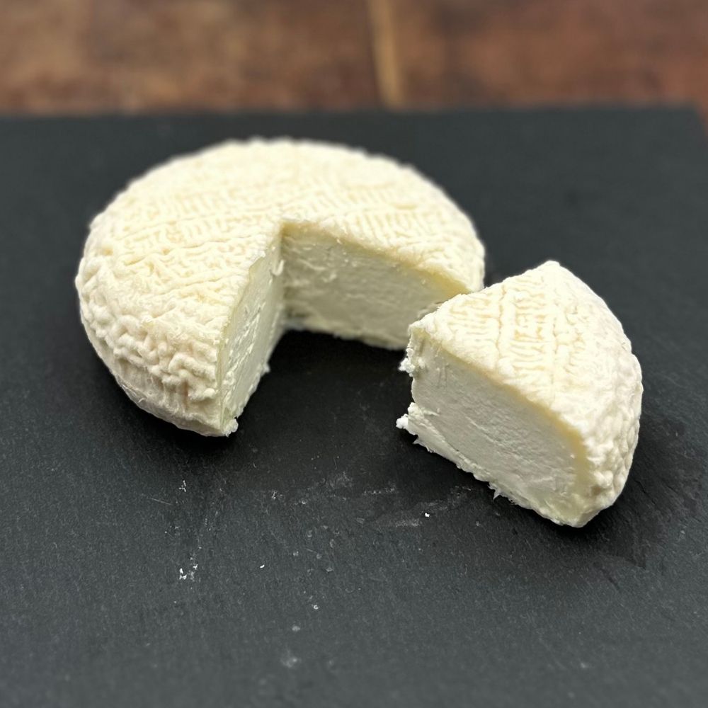 Fresh Le Fine Fleur Nature goat's cheese cut open to show its smooth, creamy interior on a black slate board.